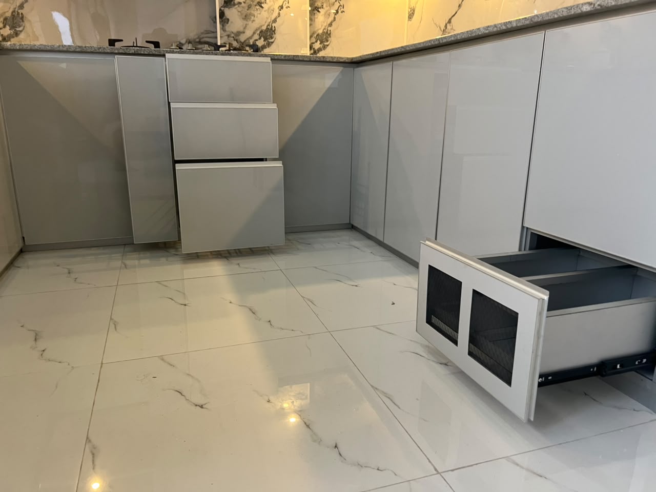 Grey gloss kitchen with open drawers and marble floor